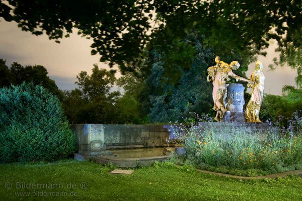 „BUNTBILD”-Nachtaufnahme vom Mozartbrunnen (Dresden). Der Mozartbrunnen ist ein Brunnen im Landschaftsgarten Bürgerwiese im Dresdner Stadtteil Seevorstadt-Ost/Großer Garten. Der Brunnen wurde vom Bildhauer Hermann Hosaeus (1875-1958), Berlin im Auftrag des Mozartvereins Dresden  von 1902 bis 1907 geschaffen. Die 3 weibl. Figuren (Anmut - Heiterkeit - Ernst) sollen die Musik Wolfgang Amadeus Mozarts in Form eines Reigens verkörpern. (Bild unter zur Hilfenahme einer LED-Taschelampe bei Nacht entstanden. Die teilweisen Unschärfen im Bild sind vom leichten Wind während der Langzeitbelichtung.)